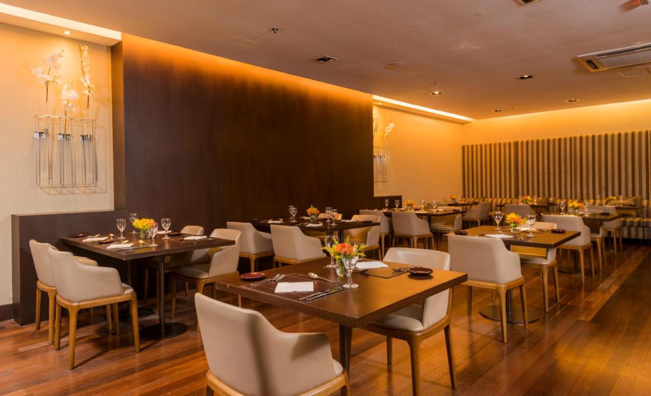 Hotel Luzeiros Sao Luis Ngoại thất bức ảnh The photo shows a modern restaurant interior. There are several tables arranged with light wooden surfaces and comfortable cream-colored chairs. Each table has a flower centerpiece and is set with tableware, including wine glasses and plates. The wal